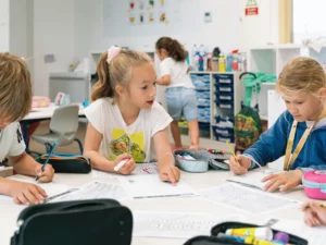 a group of children sitting at a table with paper and pencils